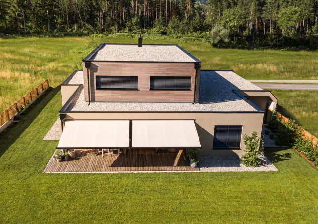 Moderne Villa mit großem Garten und Markise, umgeben von Bäumen und Wiese.