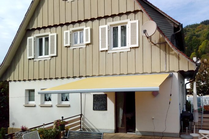 Ein helles Haus mit Awning, Lammellenfenstern und einer Treppe.