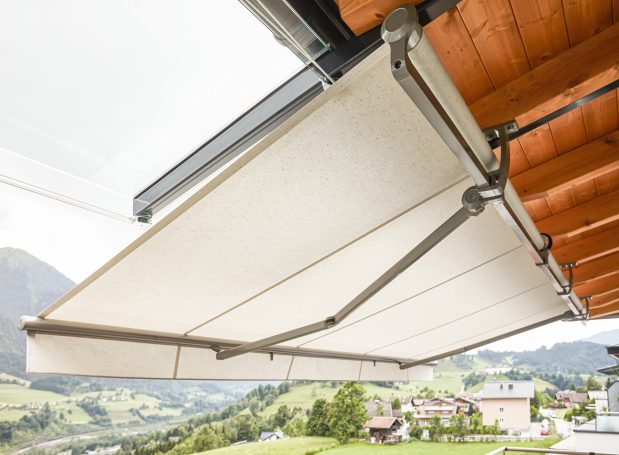 Markise mit Gestell, montiert an einem Holzüberstand, Blick auf eine grüne Landschaft.